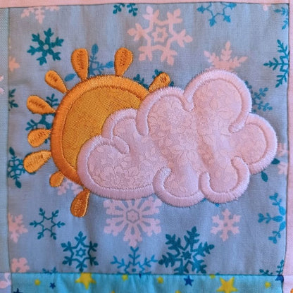 Close-up of ITH mini house quilt June embroidery design showing  appliqué sun and clouds on a fabric background.