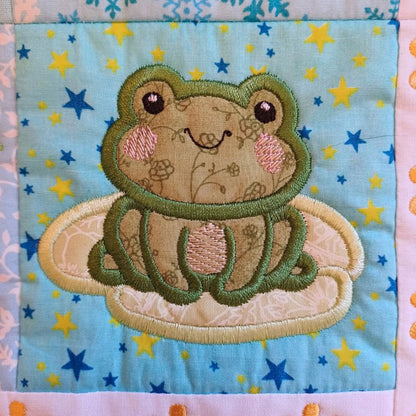 Close-up of ITH mini house quilt June embroidery design showing  appliqué frog design on a fabric background with star patterns